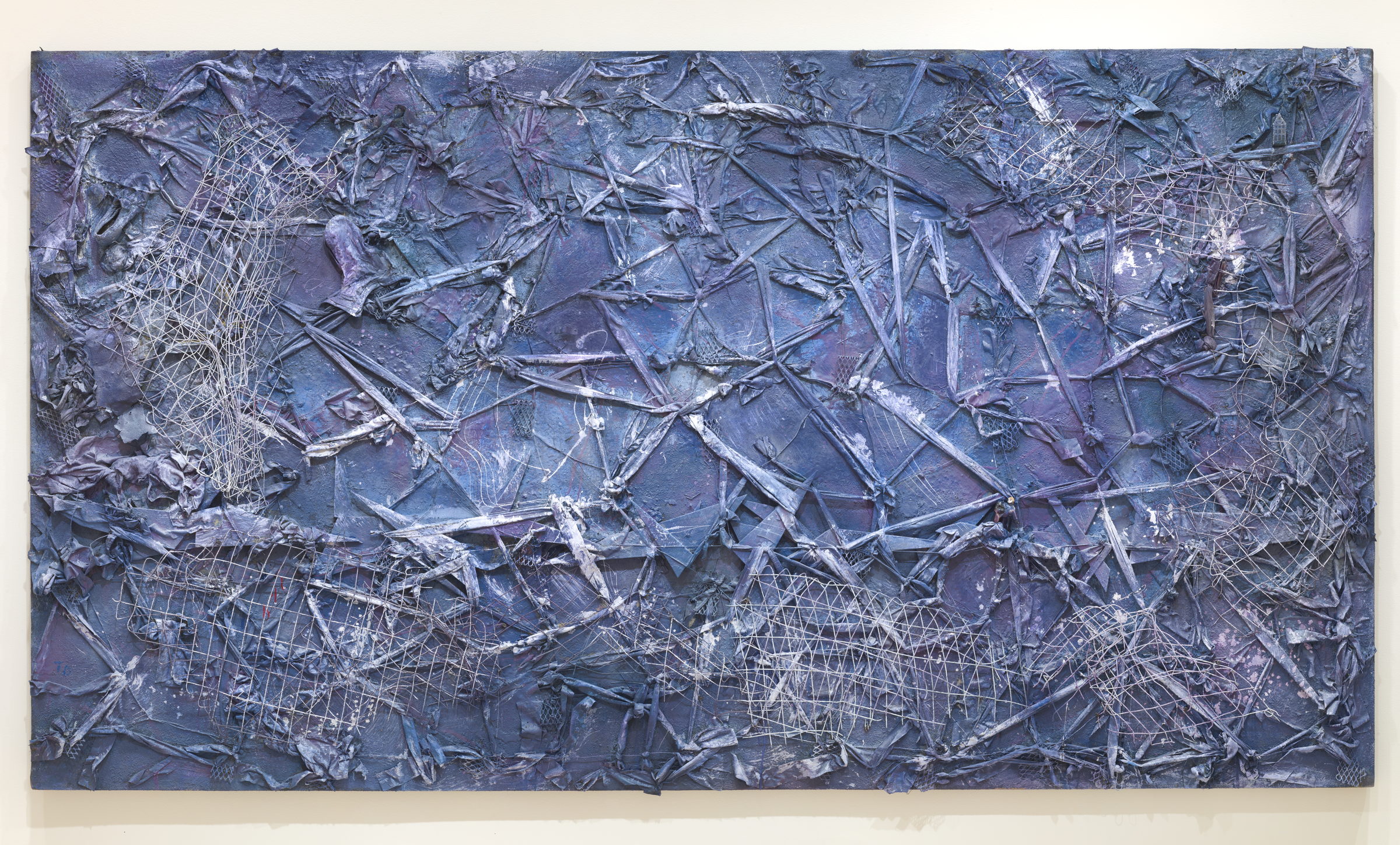 A wide horizontal panel worked over entirely in blue and violet, so that the materials read as weather rather than as objects. Torn cloth, knotted rope, wire fencing and lengths of netting are crossed and lashed over one another and painted a single colour, with paler chalky blue caught on the raised edges like foam on a swell.