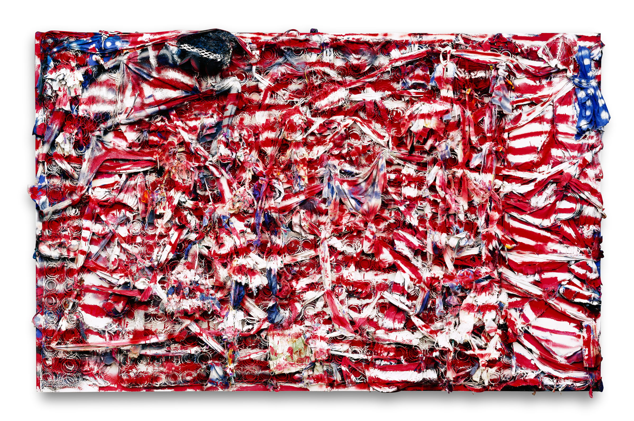 An American flag built at wall scale out of scrap. Red and white stripes are torn strips of cloth, splayed mattress coils and rows of flattened can lids, all thick with paint and pulling loose from the surface; a blue canton sits in the top left with a dark tangled mass where the stars should be, and another knot of blue cloth hangs off the right-hand edge.