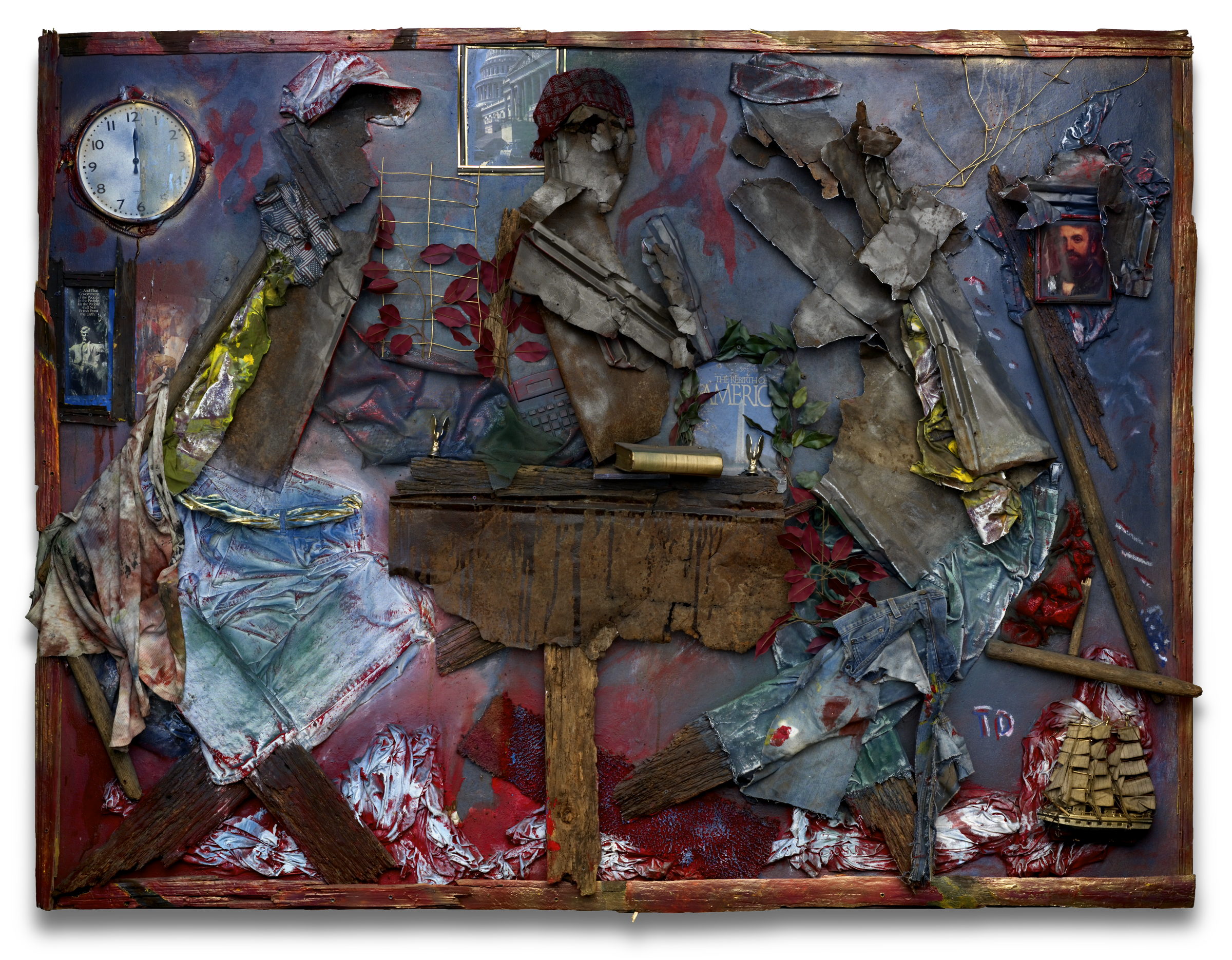 A room built in relief on a panel. Three figures made of work clothes and torn sheet metal sit at a rough wooden desk holding a book and a small keyboard. On the wall behind them hang a stopped clock, a framed photograph of the US Capitol, a small portrait and a printed card; a model sailing ship sits at the lower right, and red paint pools along the bottom edge.